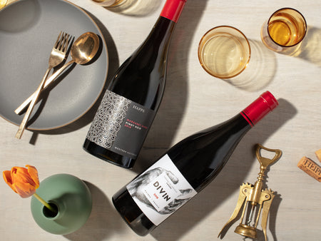 Plonk Red Wine Club image showing a couple bottles of red wine on a table with glasses, a plate with spoon and fork